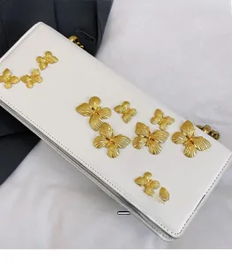 Detailed view of white faux leather crossbody bag with golden butterfly embellishments