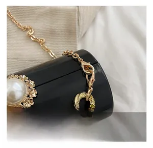 Detail of gold lobster clasp on black glossy acrylic cylinder bag with pearl floral accents