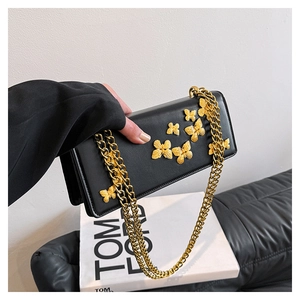 Detail of black crossbody bag featuring 3D gold butterfly charms and chunky gold chain
