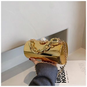 Detail view of a gold cylindrical clutch bag featuring a pearl clasp and woven chain handle