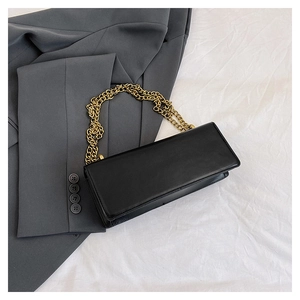Detail of black rectangular leather bag with chunky gold chain strap on grey blazer