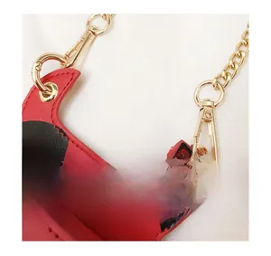 Detail of detachable gold metal chain and spring hook on red polka dot mini bag
