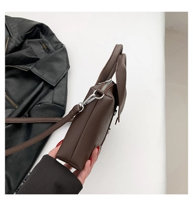 Detail view of brown lychee texture leather handbag with silver zipper and shoulder strap