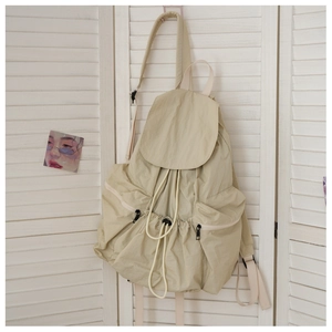 Detail view of beige nylon backpack featuring drawstring closure and side zipper pockets