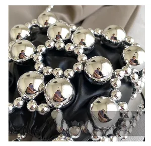 Close-up of large glossy silver beads on a black leather mini woven crossbody bag