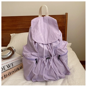 Detail view of purple nylon backpack with drawstring closure and fold-over flap on bed