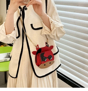 Close-up of mini red cartoon cow crossbody bag with gold chain strap on a model