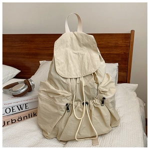 Detail of a cream pleated nylon backpack showing drawstring closure and flap design