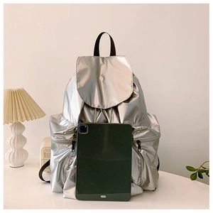 Silver metallic backpack with flap closure shown next to a tablet for size comparison