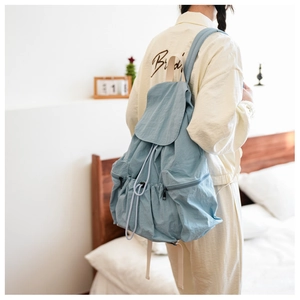 Detail of light blue nylon backpack with white drawstrings and side zipper pockets