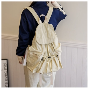 Detail of cream nylon backpack featuring drawstring closure and textured flap design