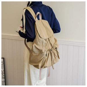 Detail of khaki pleated nylon backpack showing drawstring closure and pink straps