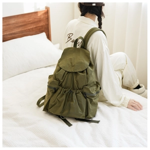 Detail of army green nylon backpack showing drawstring closure and side zipper pockets