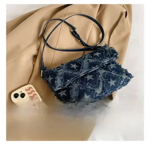 Detail view of denim crossbody bag with star patchwork and frayed edges beside a smartphone