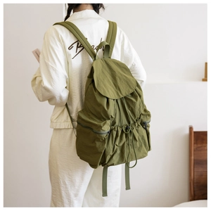 Detail of green pleated backpack with flap drawstring and side zipper pockets worn by model