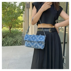 Detail of vintage blue denim crossbody bag featuring white star prints and frayed edges