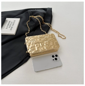 Detailed view of a gold shell clutch bag with hammer texture and a metal chain strap