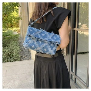 Detail view of denim shoulder bag with white star pattern and frayed tassel edges