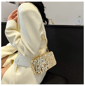 Detail of gold metallic clutch bag with ice crack texture and chain strap on a model