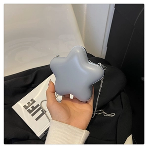 Détail d'un sac bandoulière gris en forme d'étoile avec chaîne argentée sur des livres