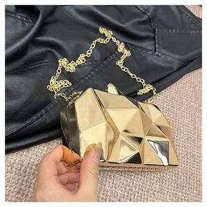 Close-up of golden geometric hardshell clutch bag with mirror finish and chain