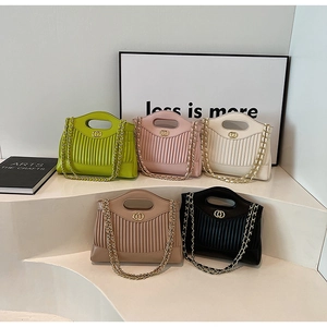 Detail of five pleated tote bags in pastel colors with gold chain straps on white podiums