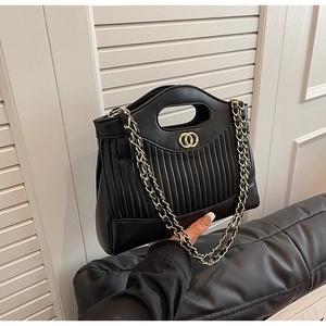 Detail of black quilted tote bag with golden circular hardware and chain strap