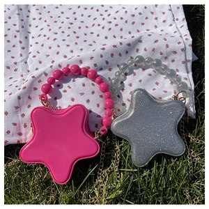 Star-shaped glitter crossbody bag with pearl handle and golden chain on a grass background