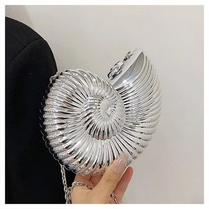 Macro view of shell-shaped silver crossbody bag with metallic spiral texture on black suit