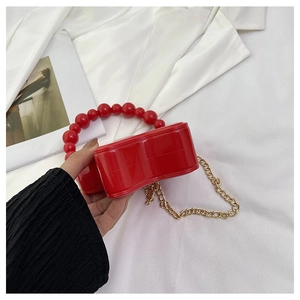 Detail of red heart-shaped hard shell bag with pearl handle and gold metal chain