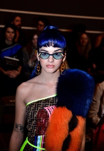 Dettaglio di occhiali da sole cat-eye con logo e orecchini a cerchio d'oro su modella