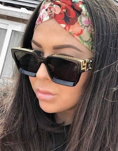 Détail des lunettes de soleil carrées noires avec motif grec doré sur les branches