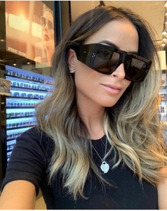 Close-up of black oversized square sunglasses with gold temple accents on a model
