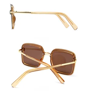 Detail view of gold metal side temples and brown lenses on square frame sunglasses