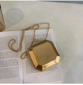 Detail of a gold octagonal metal evening bag with glossy finish and beaded chain