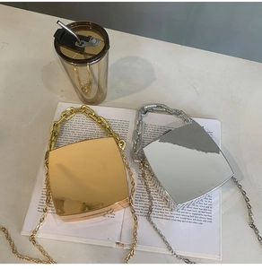 Flat lay of gold and silver mirror acrylic clutch bags with chains on a fashion book