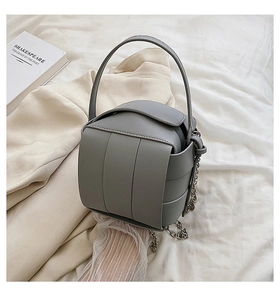 Close-up of a gray woven box handbag with a silver chain strap on a neutral background