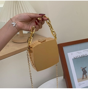 Detail of a gold mirror box clutch with chunky chain handle and sleek metallic finish