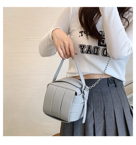 Close-up of woven patchwork box bag with silver metal chain and hand strap in light grey