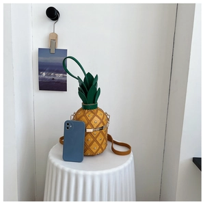 Detail of pineapple bag with gold rivets, green leaves, and metal frame closure