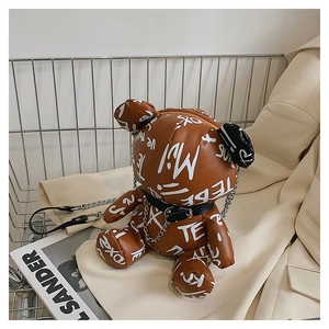 Detail of a brown bear-shaped chain bag with graffiti print resting on a beige blazer