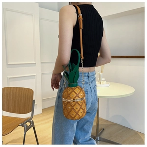 Detail of pineapple-shaped bag with rivet texture, green leaves, and gold chain strap