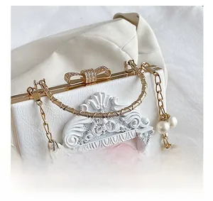 Detail of white box clutch with 3D floral relief, gold metal trim, and pearl chain strap