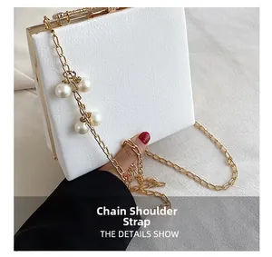 Detail of white box bag with large pearls on golden chain strap and metal clasp