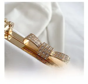 Macro detail of golden rhinestone-encrusted bow clasp on white lychee leather handbag
