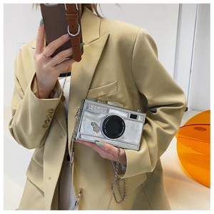 Detail of silver patent leather camera-shaped crossbody bag with metal chain strap