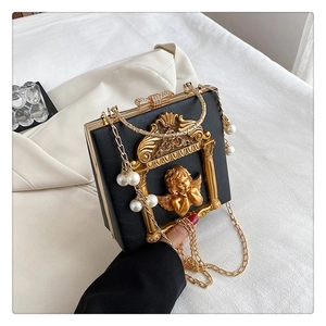 Close-up of black textured leather bag with gold baroque angel relief and pearl charm
