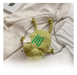 Detail showing hand-knitted green frog crossbody bag with floral accents and chain