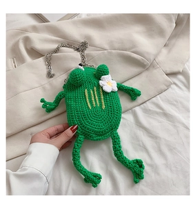 Close-up of handmade green knitted frog crossbody bag with a metal chain and white flower detail