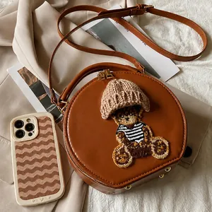 Mini bolso redondo marrón con parche de oso junto al móvil para comparar tamaños